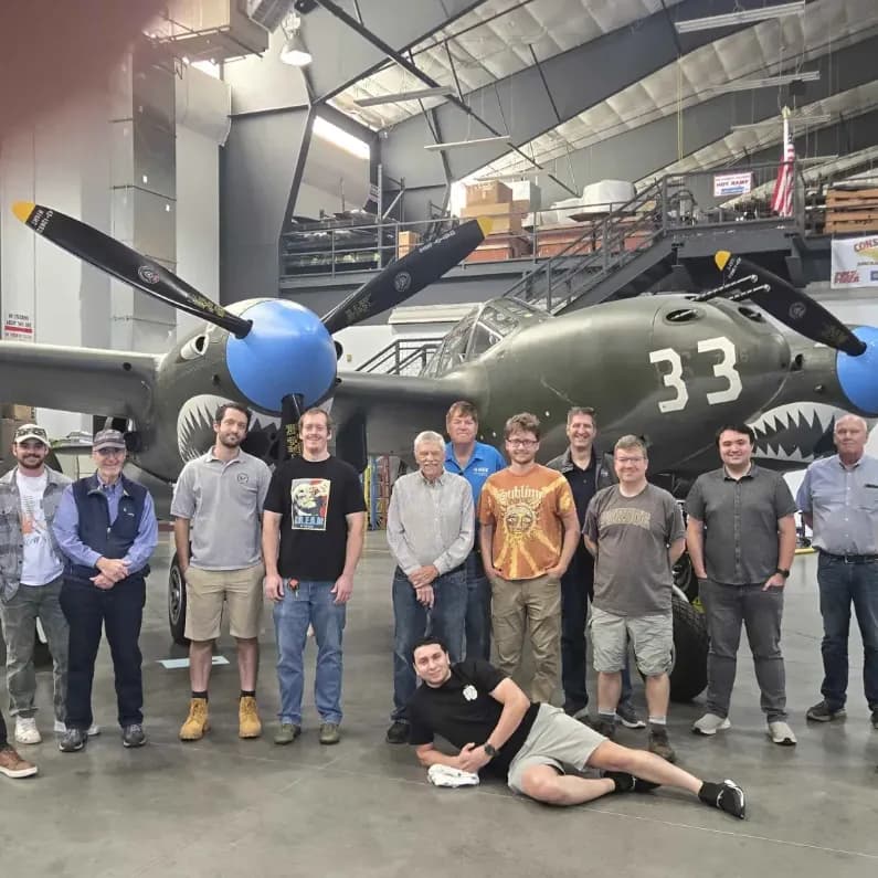Wire Lion members posing in front of a P-38 Lightning aircraft at a World War II museum