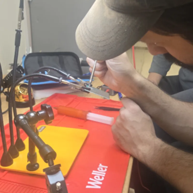 A club member soldering a circuit board held in helping hands on a red Weller mat